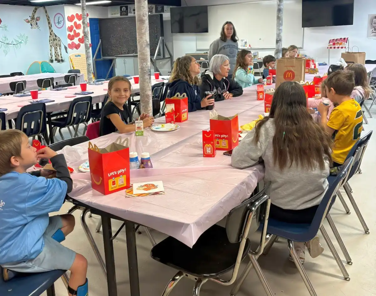 Children sitting at a decorated table enjoying a meal in a communal space.