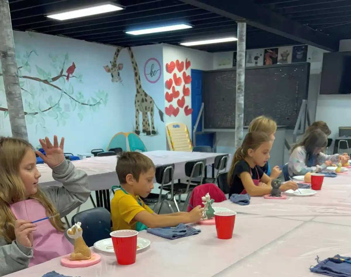 Children painting ceramics at a table with art supplies.