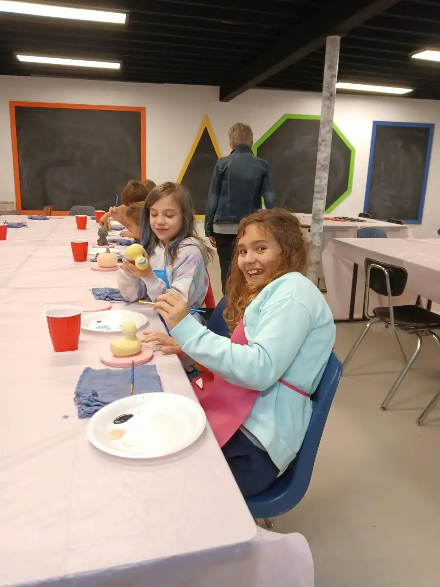 Children painting ceramics at a table with art supplies.