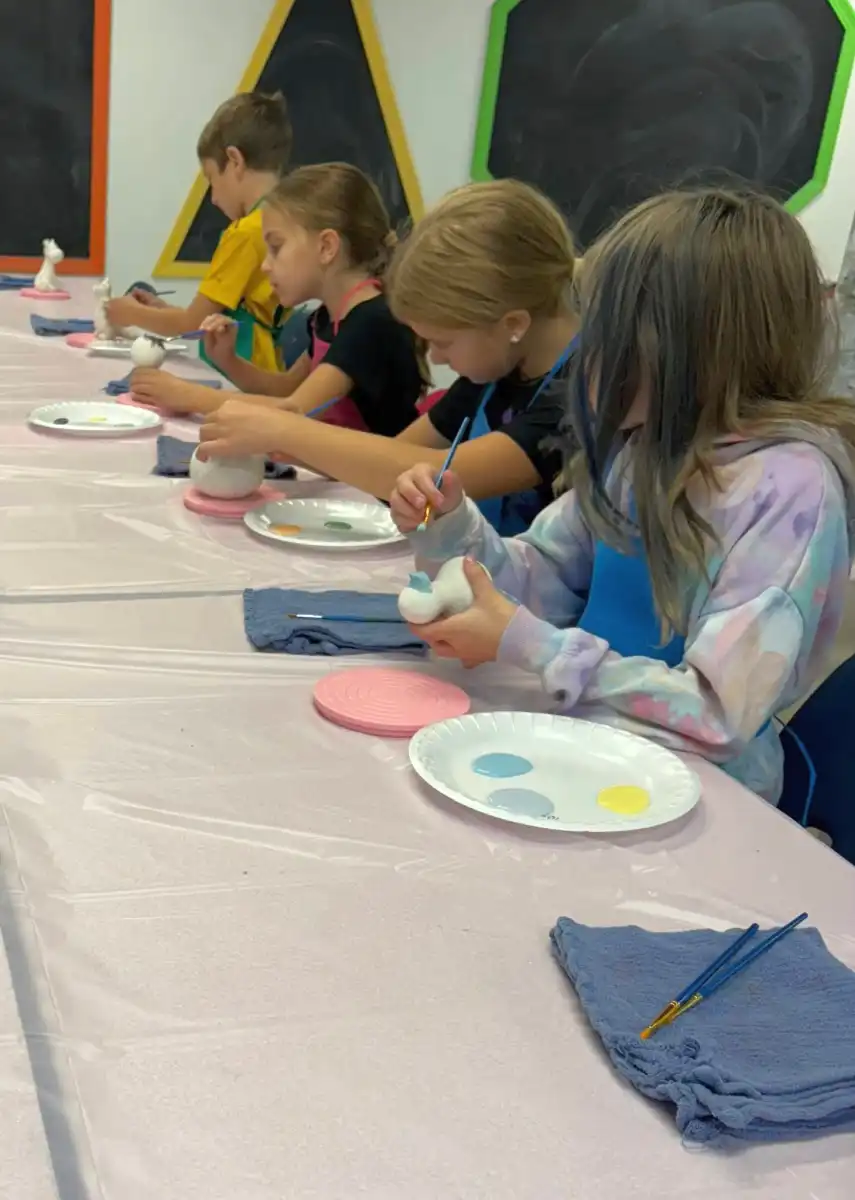 Children painting ceramics at a table with art supplies.