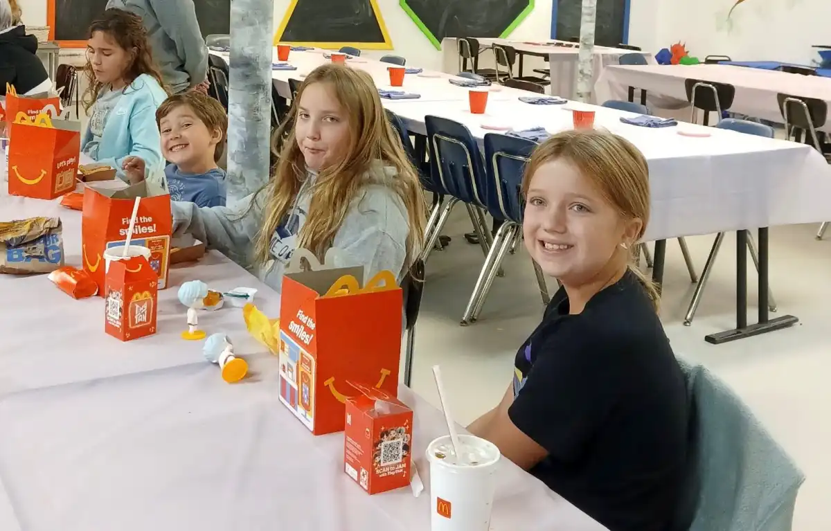 Children sitting at a decorated table enjoying a meal in a communal space.