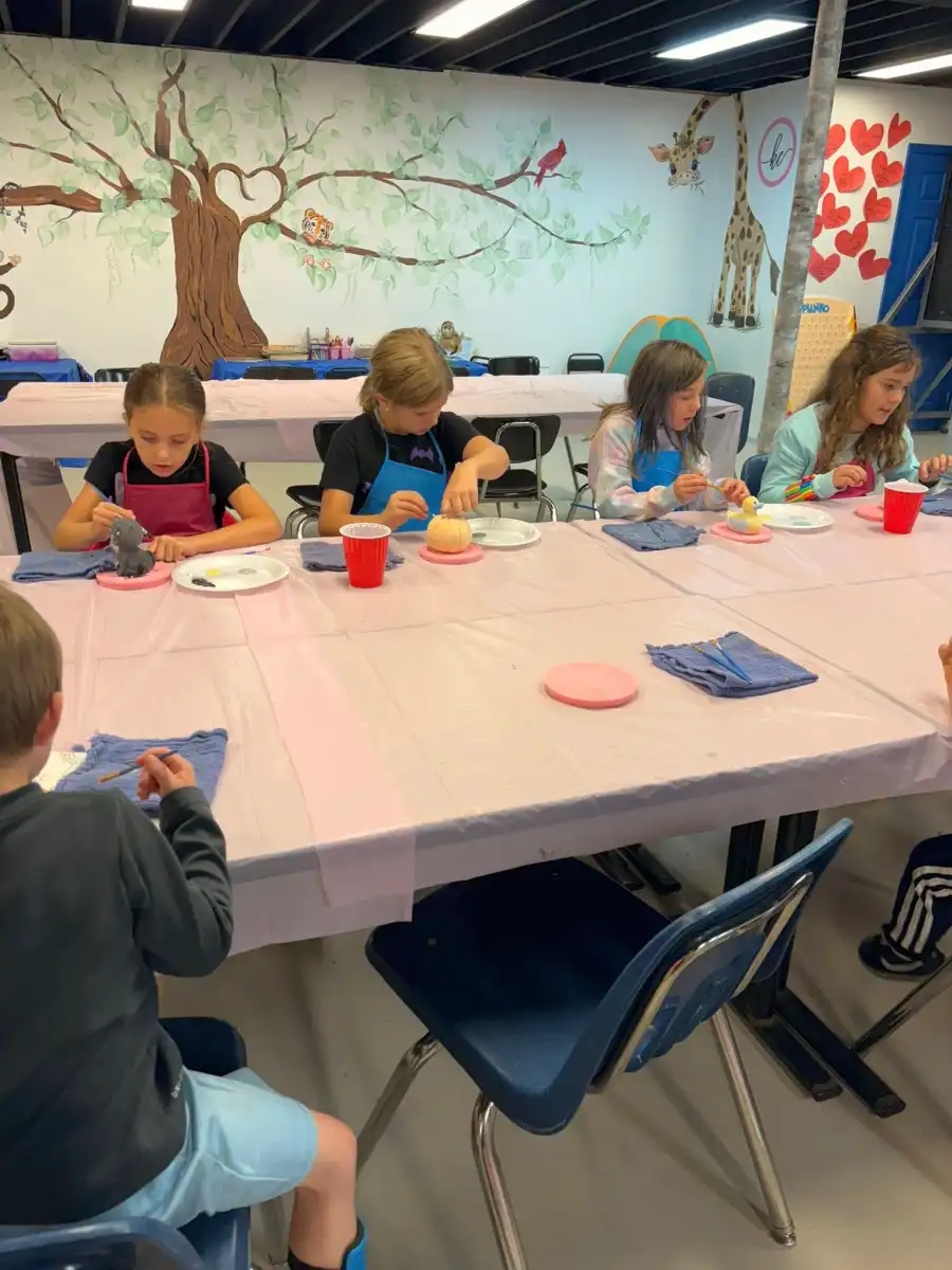 Children painting ceramics at a table with art supplies.