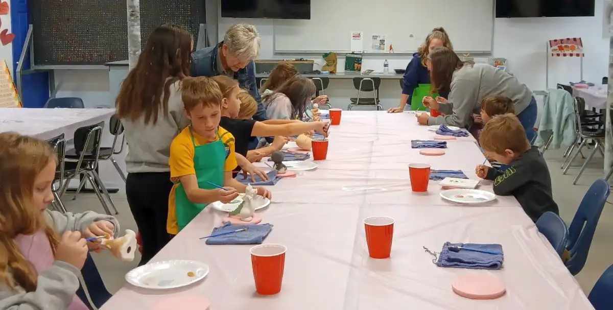 Children painting ceramics at a table with art supplies.